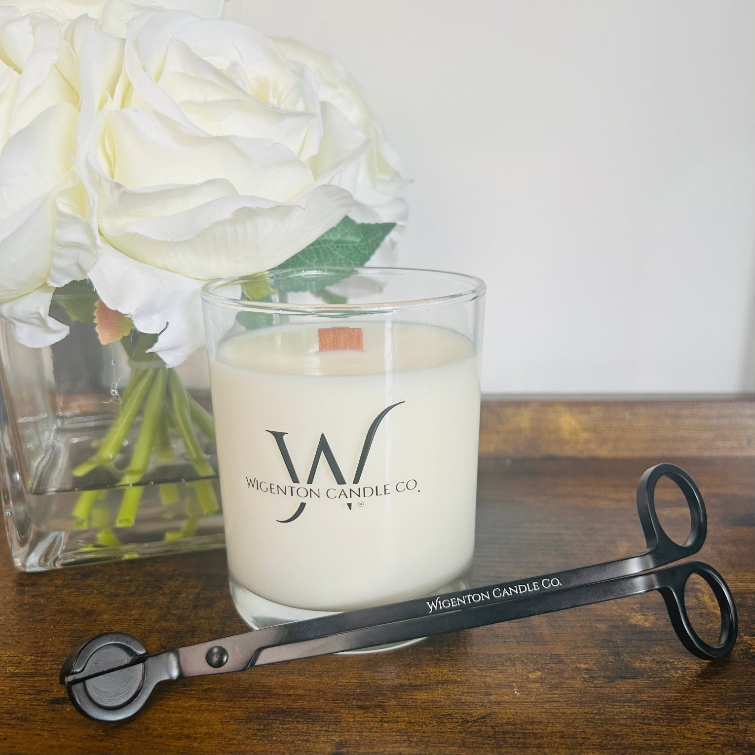 Wigenton Candle Co. candle with a matte wick trimmer that we sell and flowers on a wooden surface