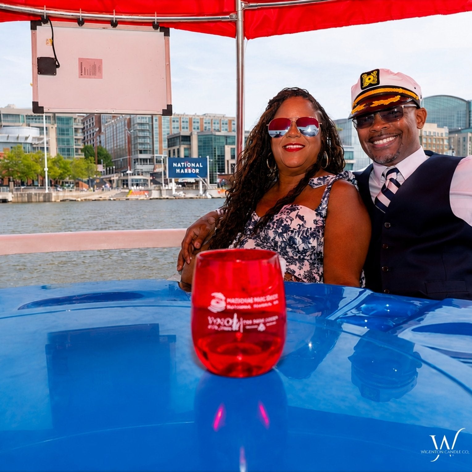Couple smiling on a red canopy donut boat at National Harbor during a Wigenton Candle Co. Scent & Sail experience.