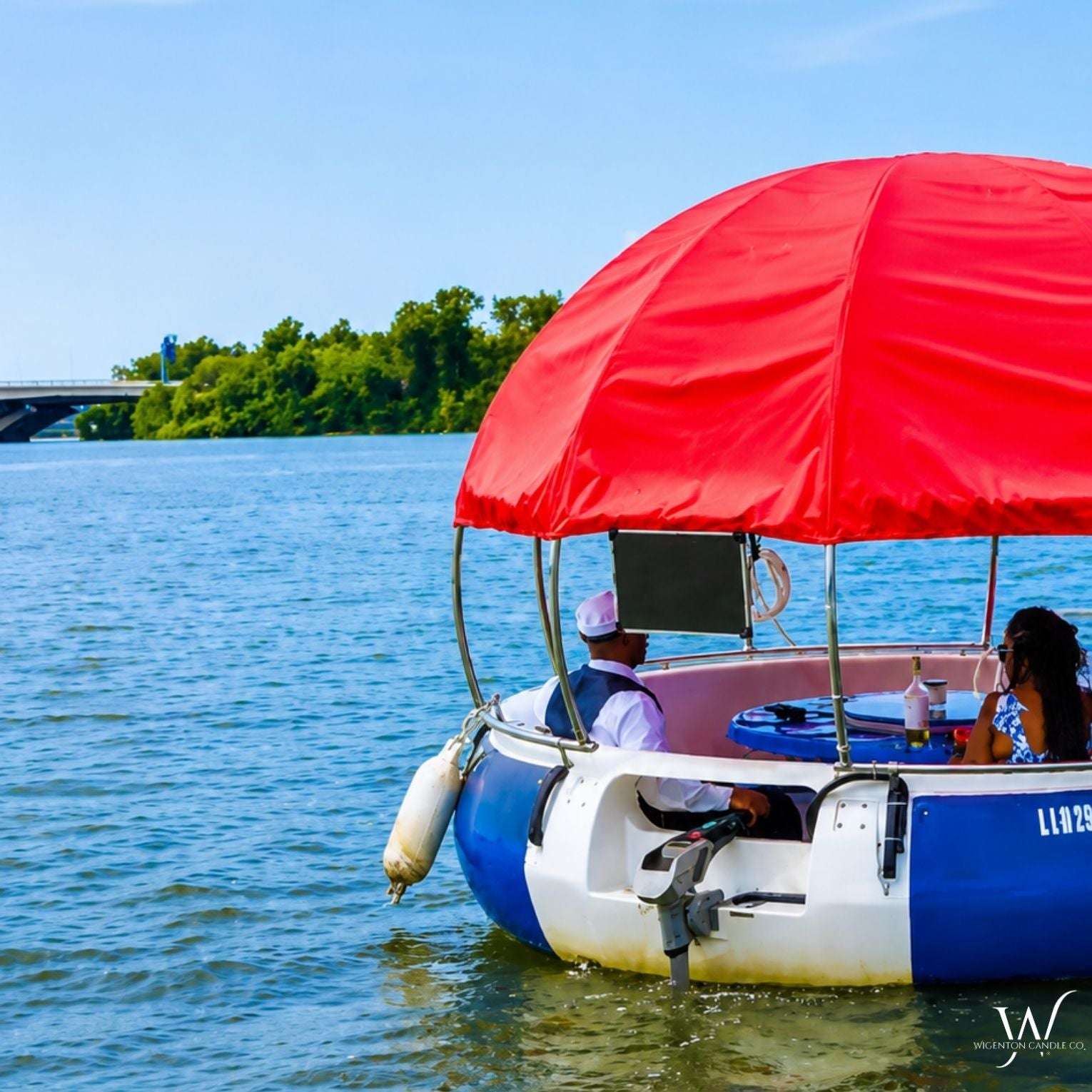 Two guests relaxing on a red canopy donut boat on the water during a Wigenton Candle Co. Scent & Sail experience.