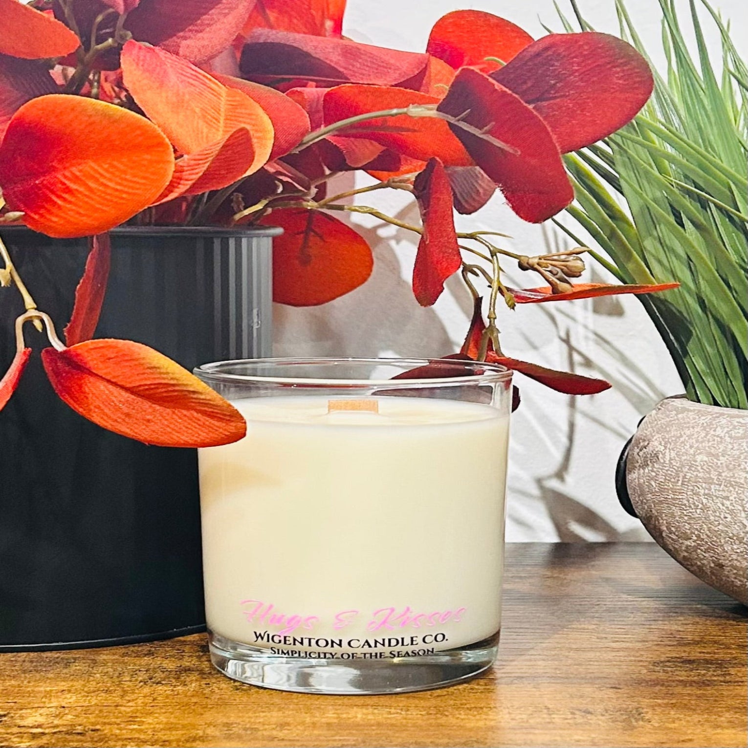 Glass candle with visible Wigenton Candle Co brand name on a wooden surface with plants in the background