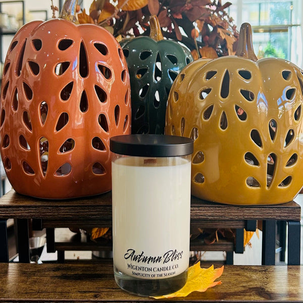 Candle labeled 'Autumn Bliss' with three ceramic pumpkins in the background.