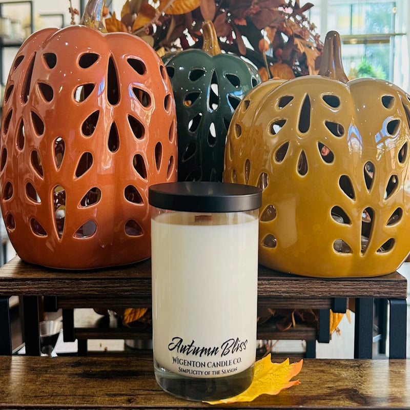 Candle labeled 'Autumn Bliss' with three ceramic pumpkins in the background.