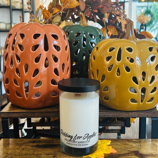 Candle with 'Bobbing for Apples' text in front of ceramic pumpkins on a wooden surface - Wigenton Candle Co. fragrance.
