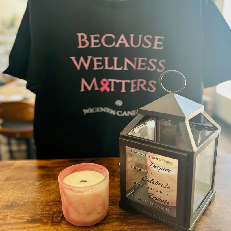 Black t-shirt with 'Because Wellness Matters' text, Cozy scented candle, and lantern with custom message on a wooden surface.