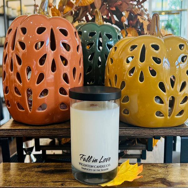 Candle labeled 'Fall in Love' with decorative ceramic pumpkins in the background.