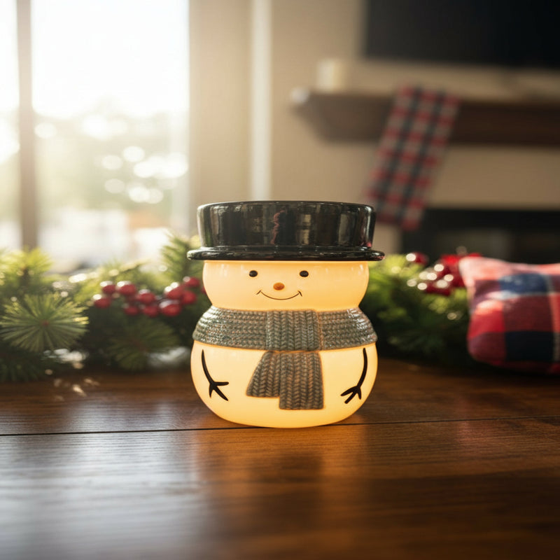 Snowman fragrance warmer with soft golden light glowing from inside, sitting on a wooden table in a cozy holiday living room