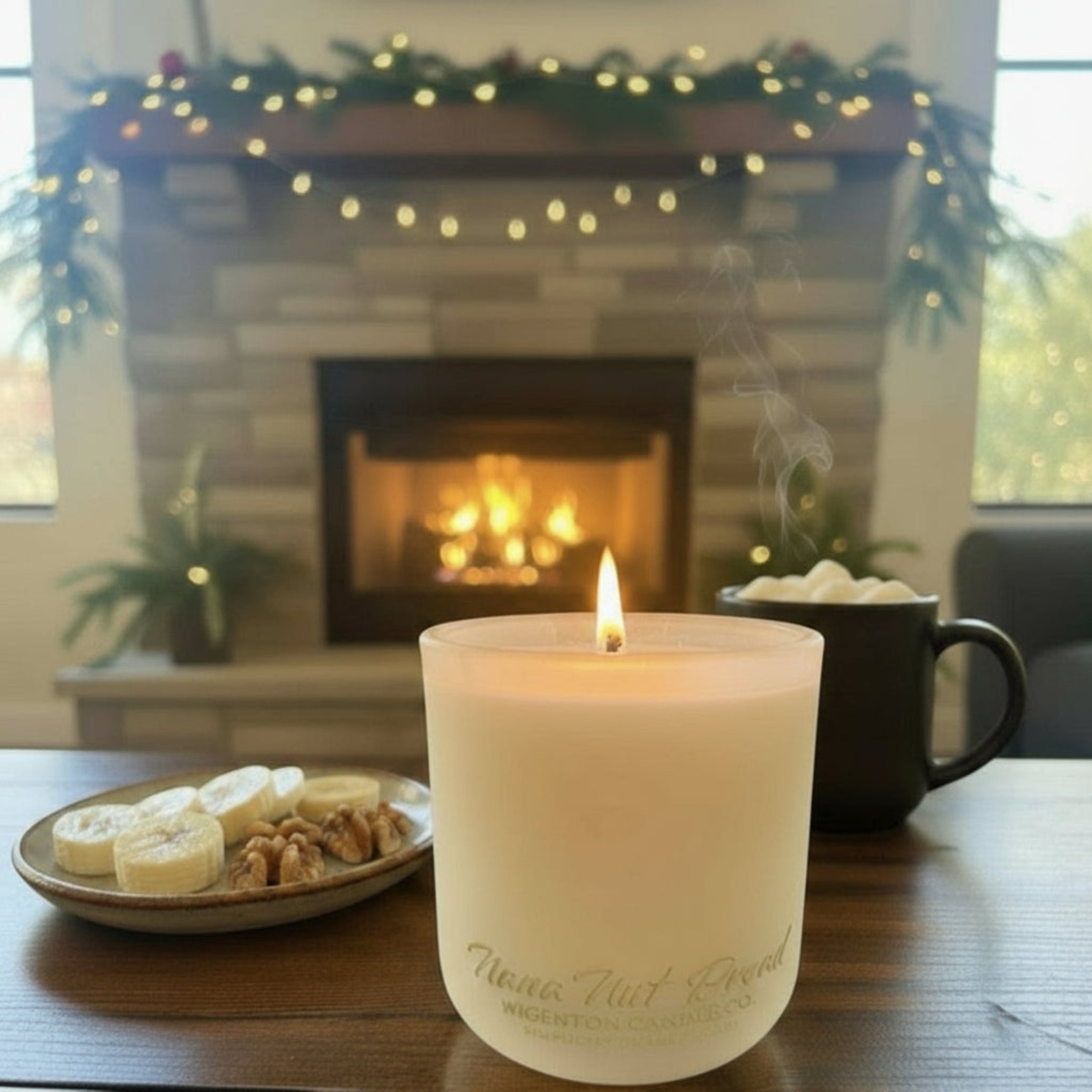 Nana Nut Bread candle with flame on a wooden table beside a subtle steaming mug of hot cocoa, with a fireplace and garland in the background for a cozy holiday atmosphere.