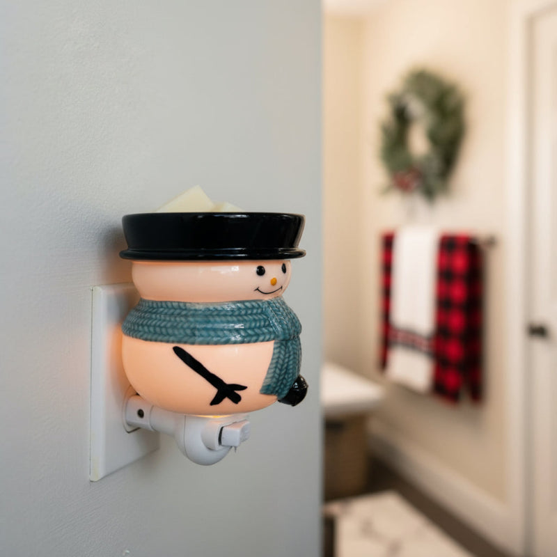 Snowman pluggable fragrance warmer with wax cubes plugged into wall outlet in cozy holiday setting