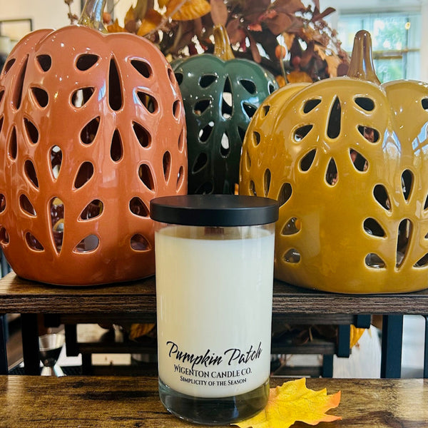 Candle labeled 'Pumpkin Patch' by Wigenton Candle Co. in front of decorative ceramic pumpkins.