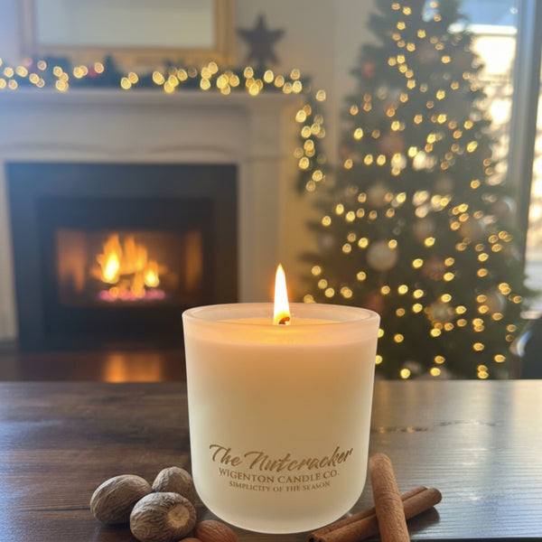 The Nutcracker wooden wick soy candle from Wigenton Candle Co. glowing on a wooden table with cinnamon and nutmeg beside it in a cozy holiday living room