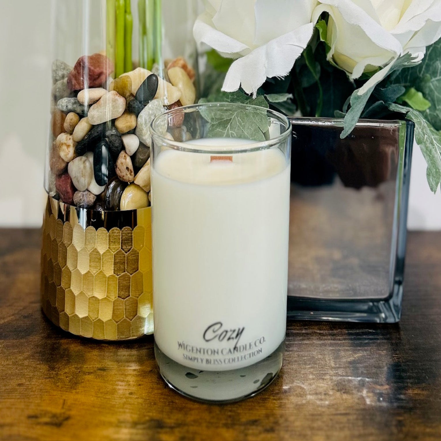 Soy Candle labeled 'Cozy' with decorative jars and flowers on a wooden surface